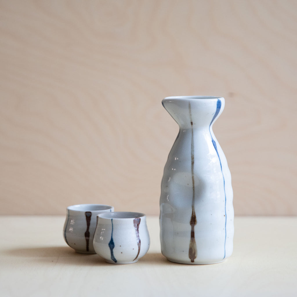 Set of white ceramic sake cups and jug with hand painted vertical lines in blue and brown. This set in made in Japan.