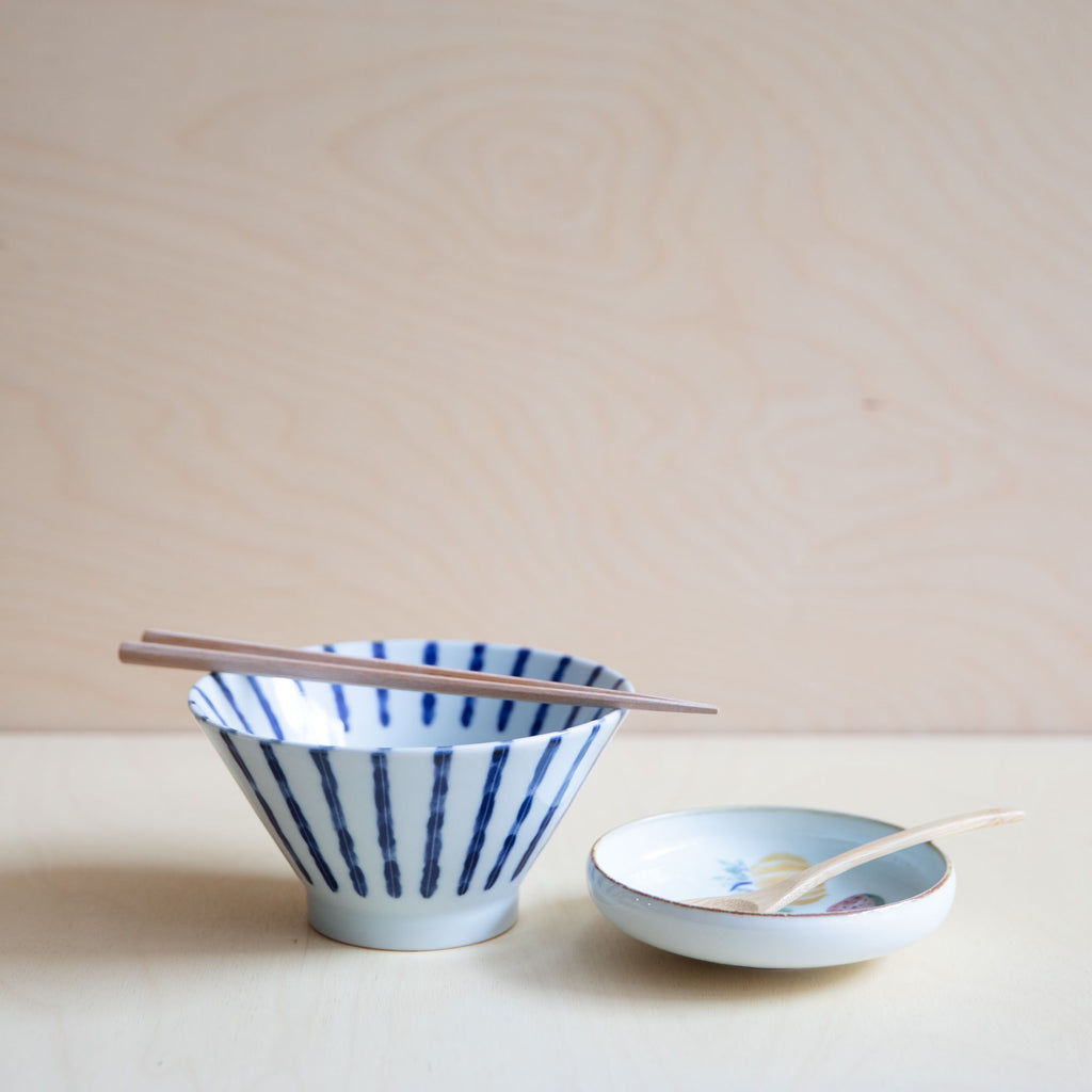 white bowl with blue vertical lines with wooden chopsticks and a small dish