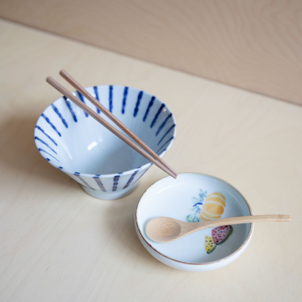 white bowl with blue vertical lines paired with wooden chopsticks and a small dish with a wooden spoon