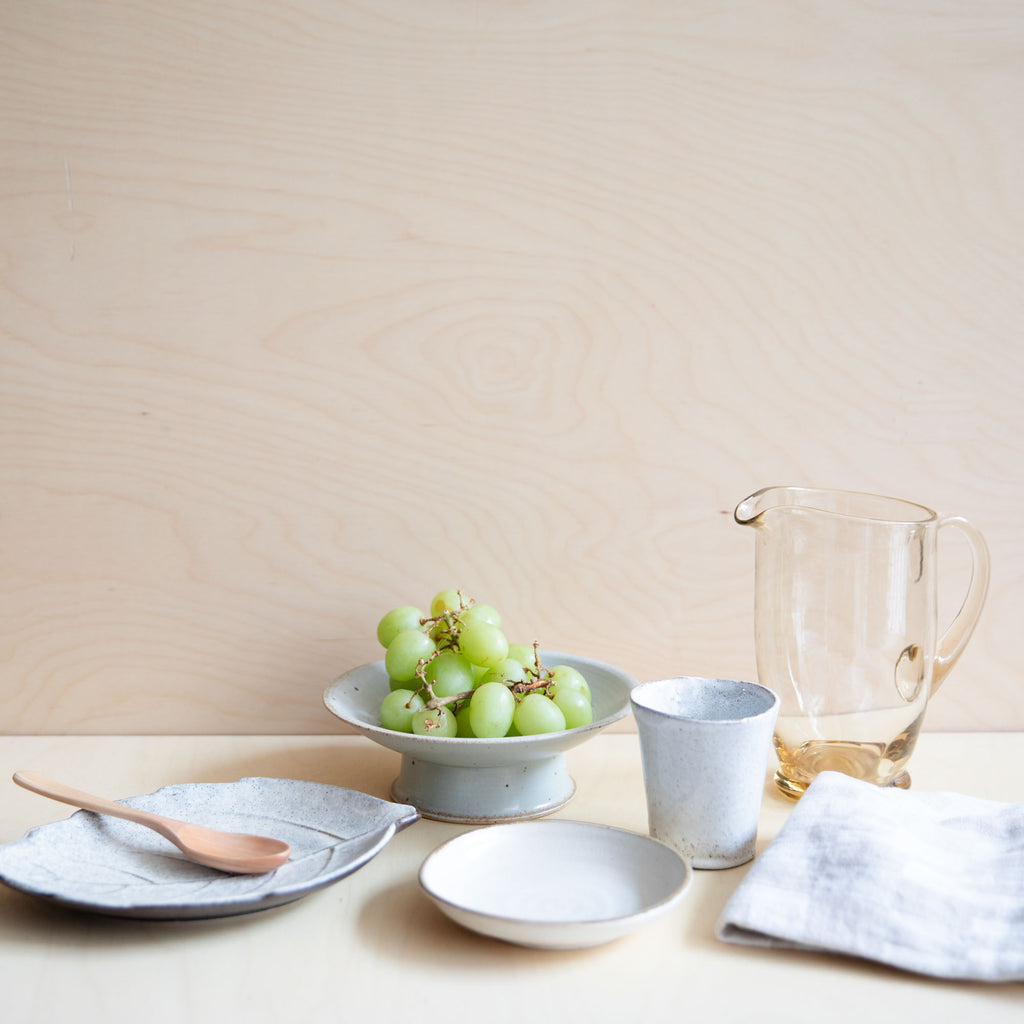 leaf plate with in a table setting with glass jug and cups and plates and grapes